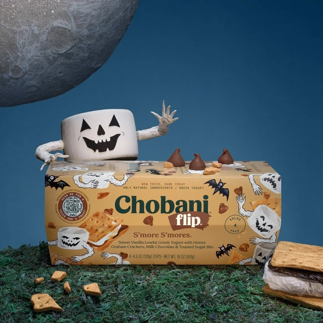 Chobani S'more S'mores yogurt carton with Halloween marshmallow character and graham cracker, chocolate treat, blue backdrop.