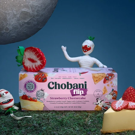 Chobani Flip Strawberry Cheesecake yogurt with Halloween mummy figurines, strawberry props, and spooky lunar backdrop in studio setting.