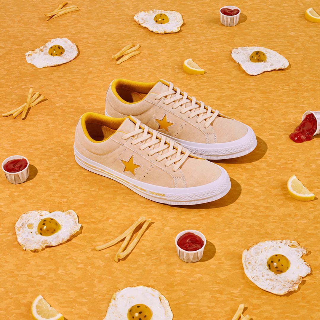Sneakers still life. Low-top beige Converse One Star sneakers with a yellow star, arranged with fried eggs, fries and ketchup cups.