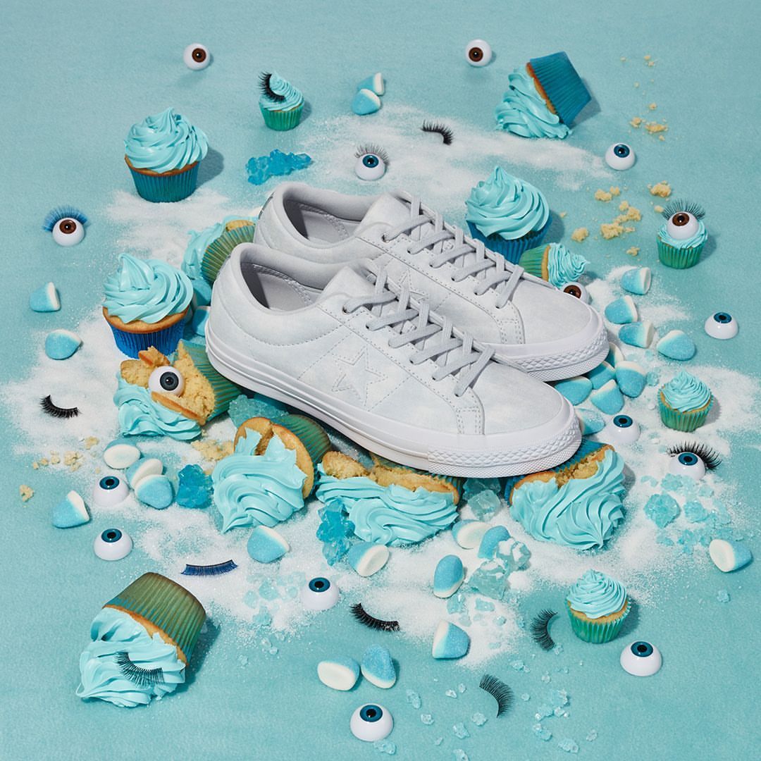 A pair of white sneakers surrounded by blue frosted cupcakes, blue gelatin candies, fake eyelashes, and toy eyeballs on a light blue backdrop.