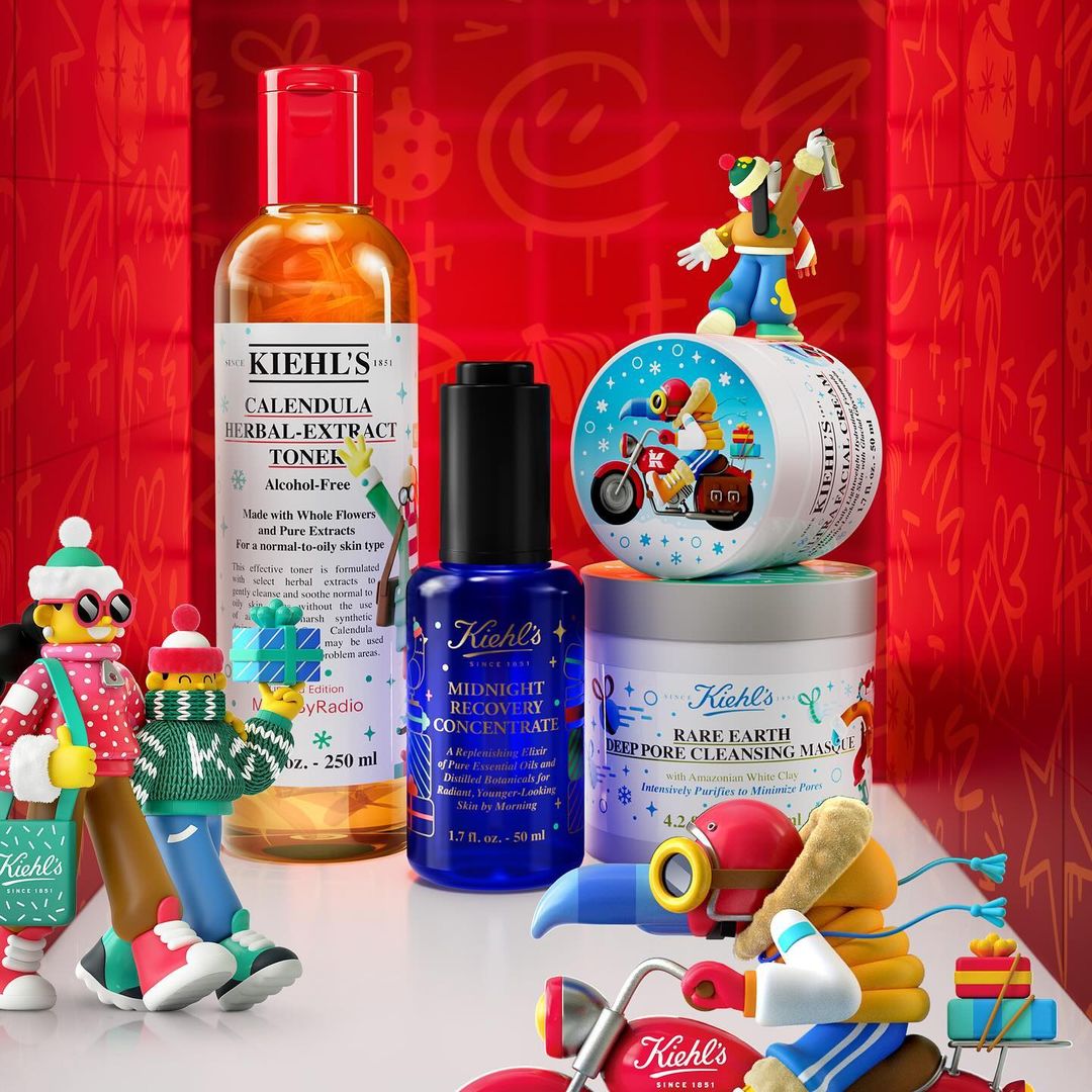 Still life featuring Kiehl's skincare products against a red patterned backdrop, including toner, concentrate, and mask jars, with toy figures.