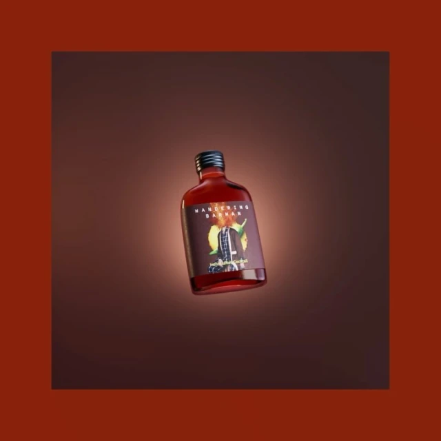 A close-up studio shot of a red liquid in a small glass bottle with a black cap, showcasing its label against a warm brown backdrop.