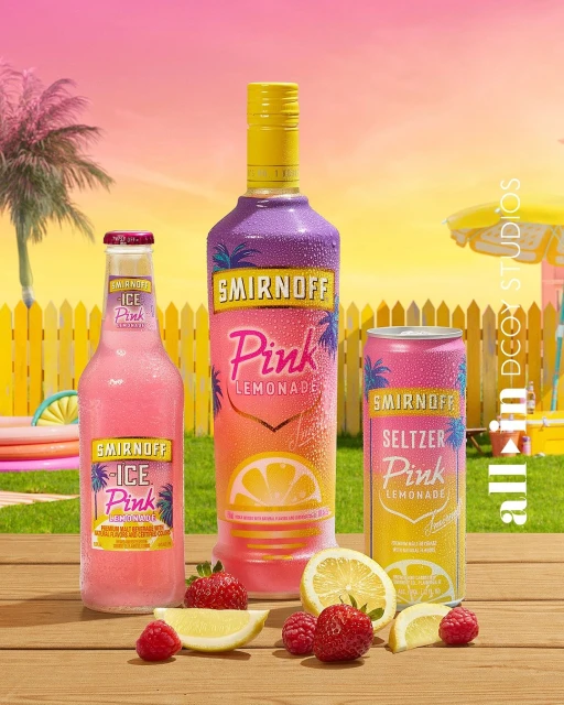 Smirnoff Pink Lemonade beverages including a bottle, can, and ice drink are arranged with strawberries and lemons on a wood surface.