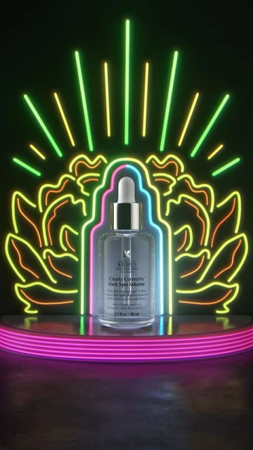 Still life shot of a Kiehl's corrective dark spot solution bottle on a illuminated display, highlighted with neon lights against a black background.