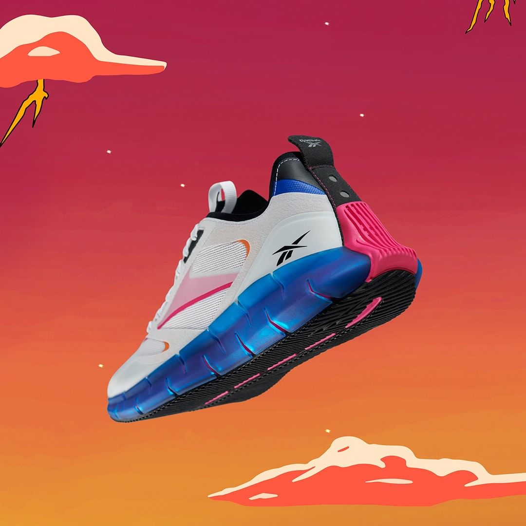 Studio shot of a white Reebok sneaker with blue and pink accents, hovering in the air against an illustrated orange and red background.