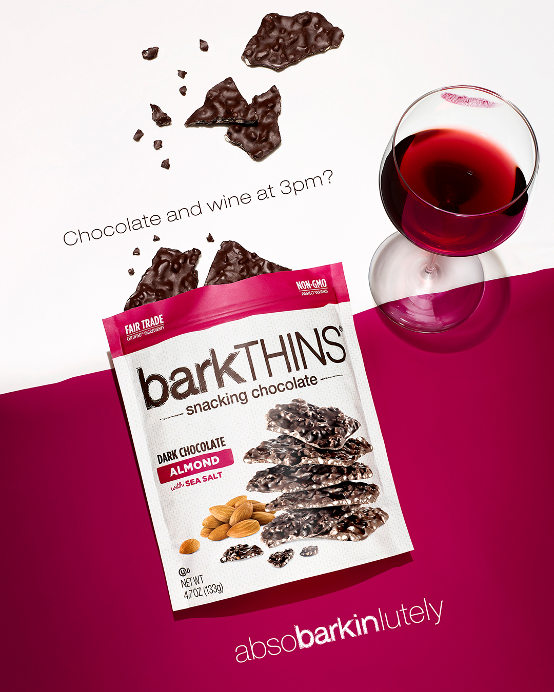 BarkTHINS snacking chocolate and a glass of red wine sit on a split white and fuchsia surface in a brightly lit studio shot.