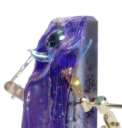Close-up of a blue and purple resin sculpture on a silver and gold metal stand, displayed against a stark white background.