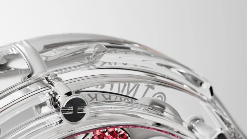Close-up of a transparent sphere with metallic structures and red jewels, set against a clean, bright background, showcasing its intricate design.