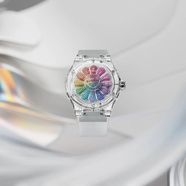 Elegant watch with a transparent band and a rainbow-colored, flower-shaped face, set against a bright, rippled reflective background.
