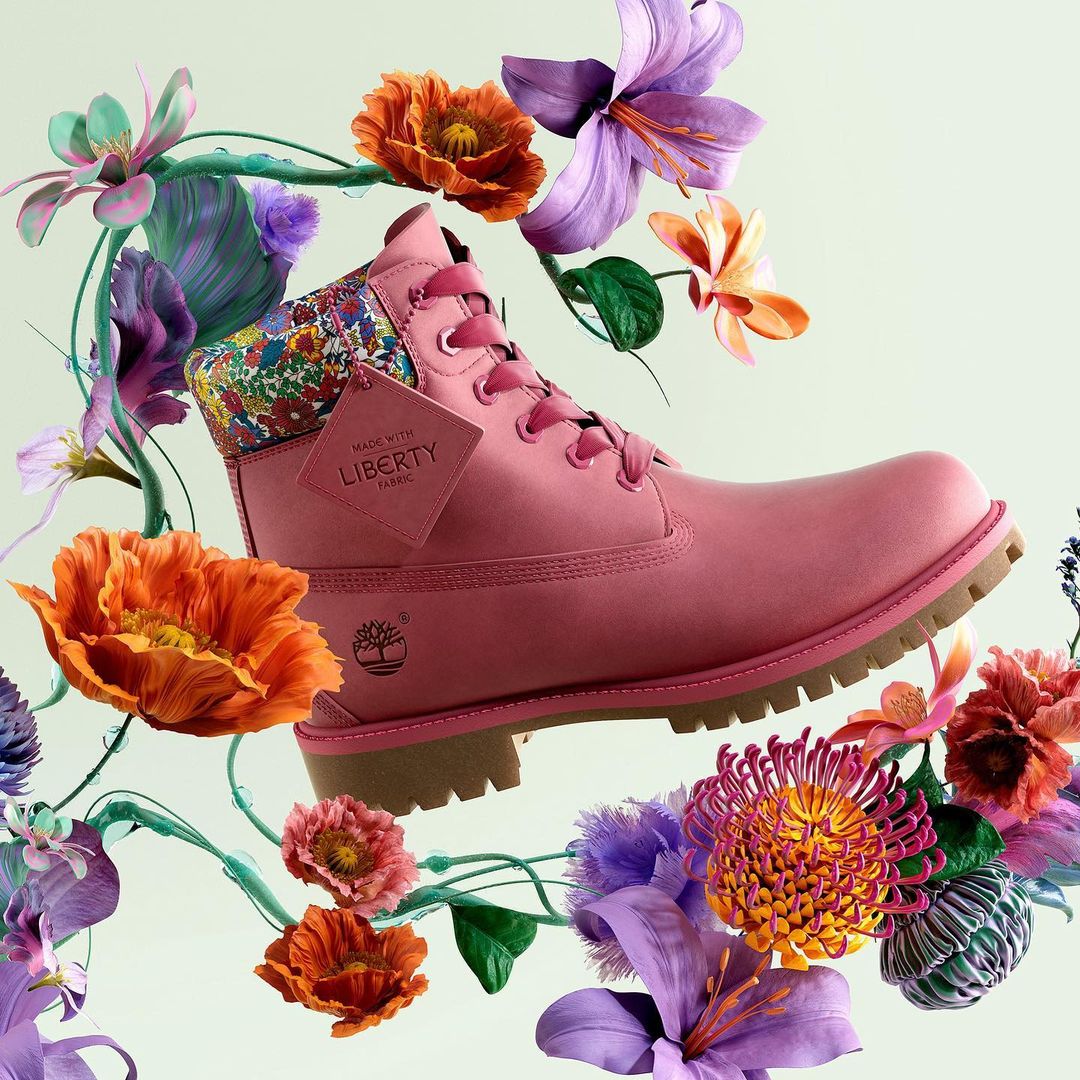 Pink Timberland boot floating in mid-air, surrounded by colorful spring flowers in full bloom, set against a light green backdrop.