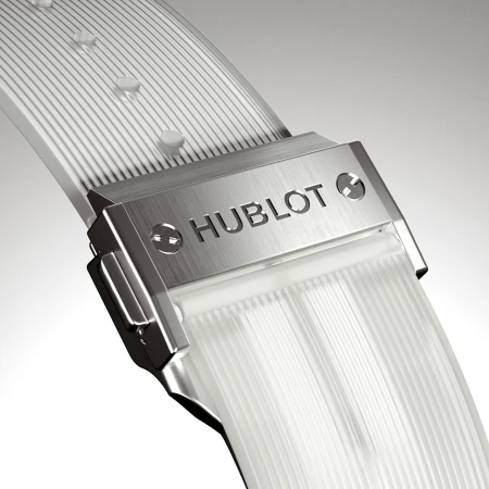 Close-up of a Hublot watch buckle and clear band showing the brand name against a neutral gradient background in a studio shot.