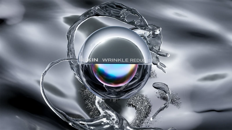 Still life product shot of wrinkle reducing cream in a clear container surrounded by water droplets on a silver reflective surface.