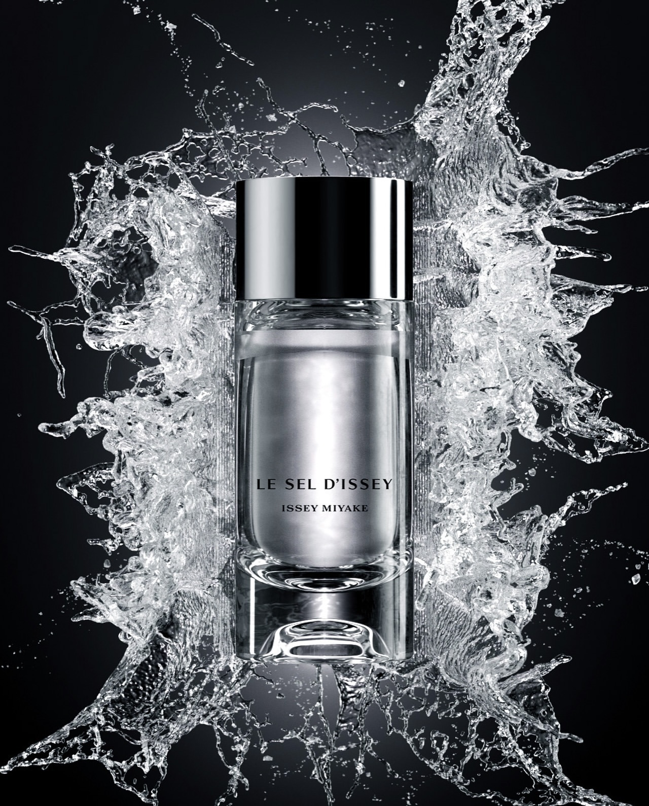 A cylindrical glass perfume bottle surrounded by a frozen splash of water against a dark black background.