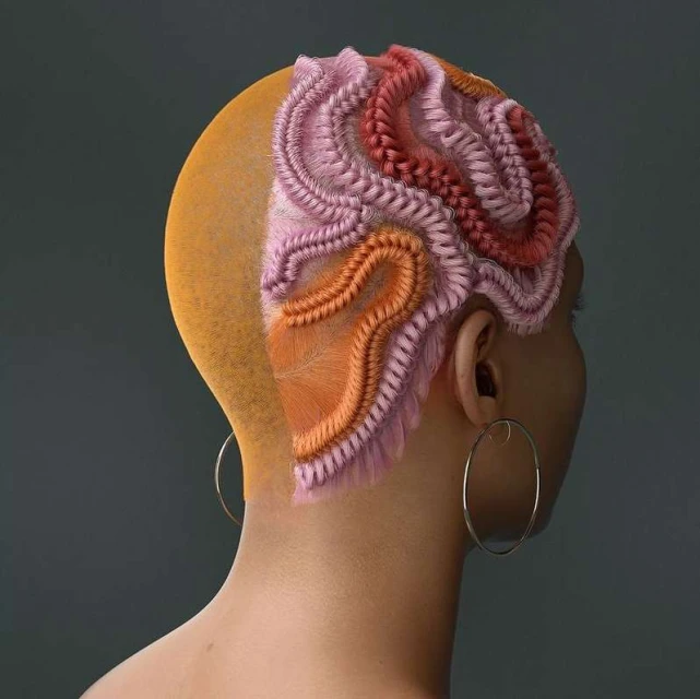 Artistic hairstyle with pink, red, and orange braids on a woman with a shaved head against a grey background; hoop earring visible.