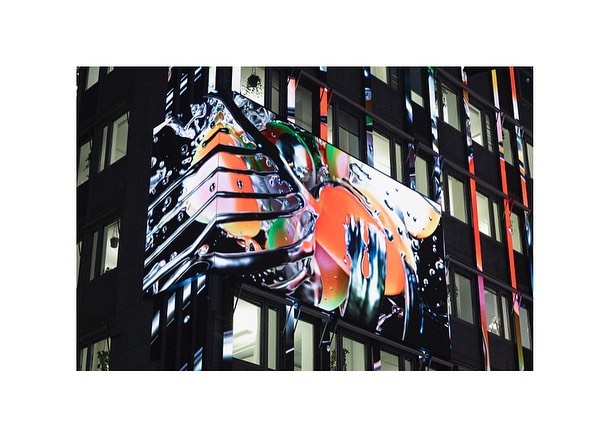 Architectural building with colorful abstract art installation on corner, featuring reflective surfaces and black framework.