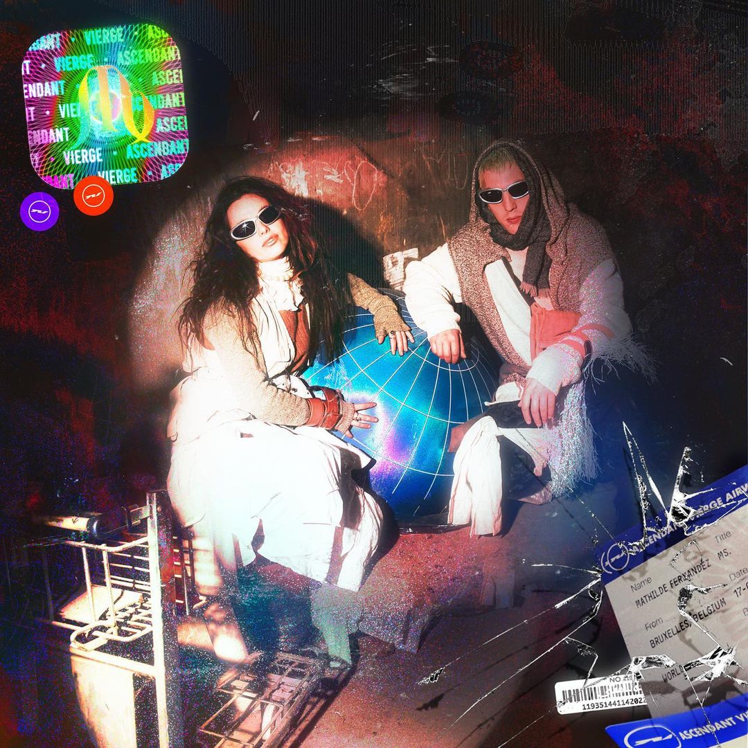 Two people sit on an illuminated blue globe indoors with retro film grain, featuring a woman with long hair and a man with sunglasses.