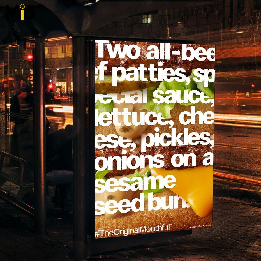 Burger advertisement on a bus stop at night. The poster features stacked burger ingredients over-layed with white text.