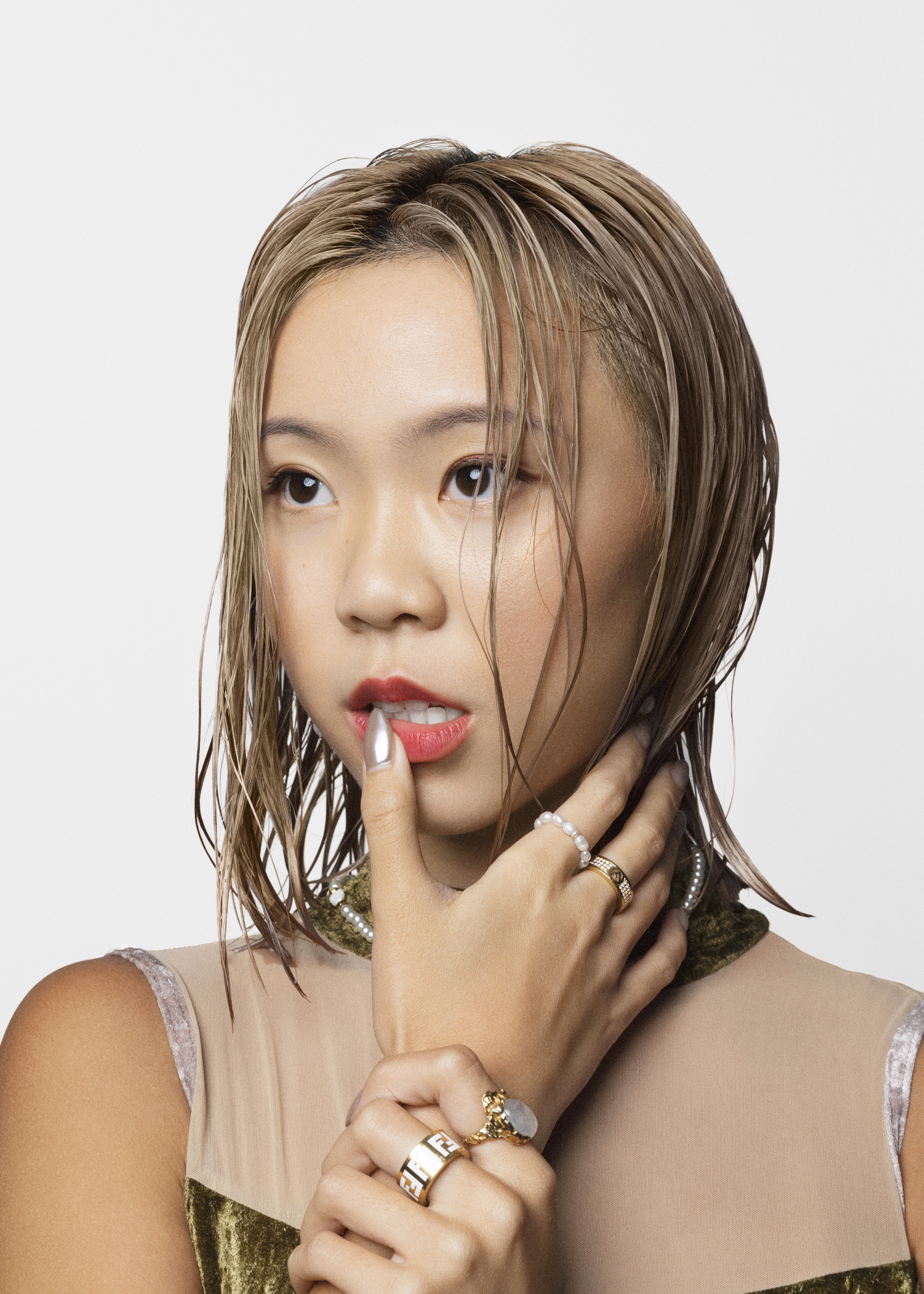 Close-up portrait of a young adult female with wet blonde hair, red lipstick, and rings, posing in a photo studio against a white backdrop.