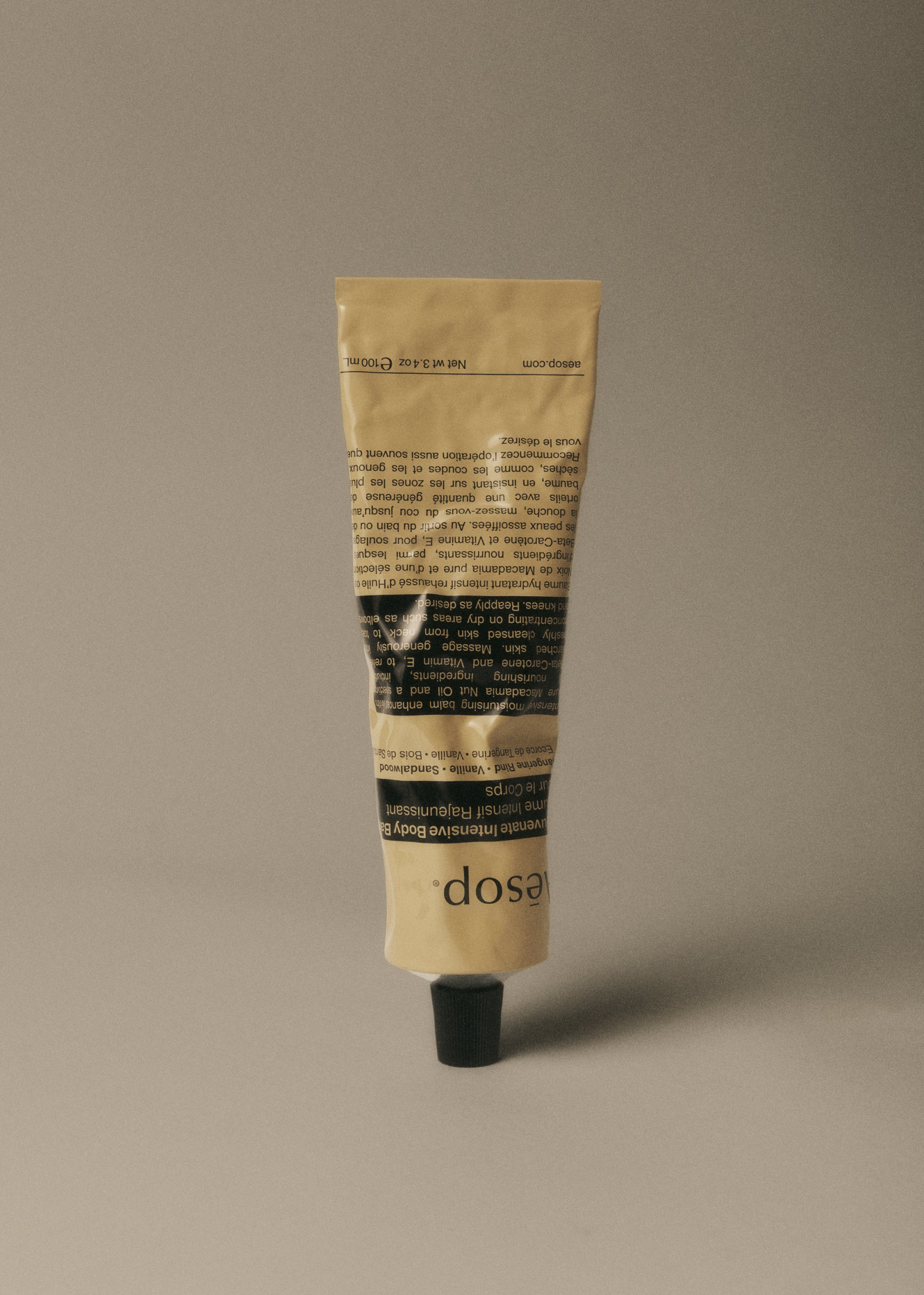 Aesop hand cream in a beige tube with a black cap on a grey background. Cream tube is standing. Copy and logo on the label.