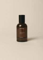 Amber glass perfume bottle with black cap against a pale neutral background