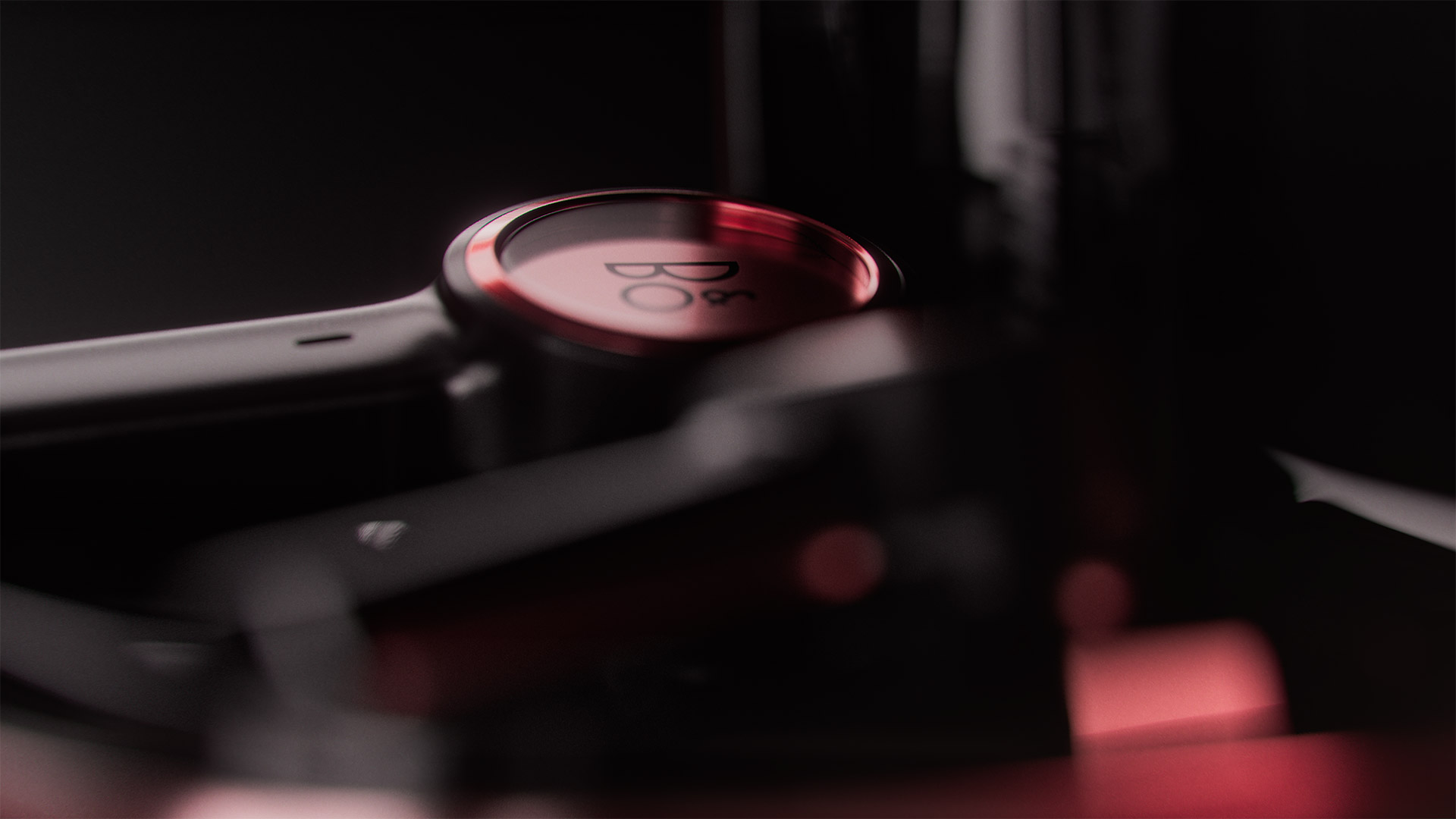 Close-up shot of Bang & Olufsen (B&O) wireless headphones featuring the logo. The headphones are dark with red and black accents.
