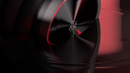 Close-up product shot of a sleek black over-ear headphone with red lighting accents and metallic textures reflecting on a glossy dark surface