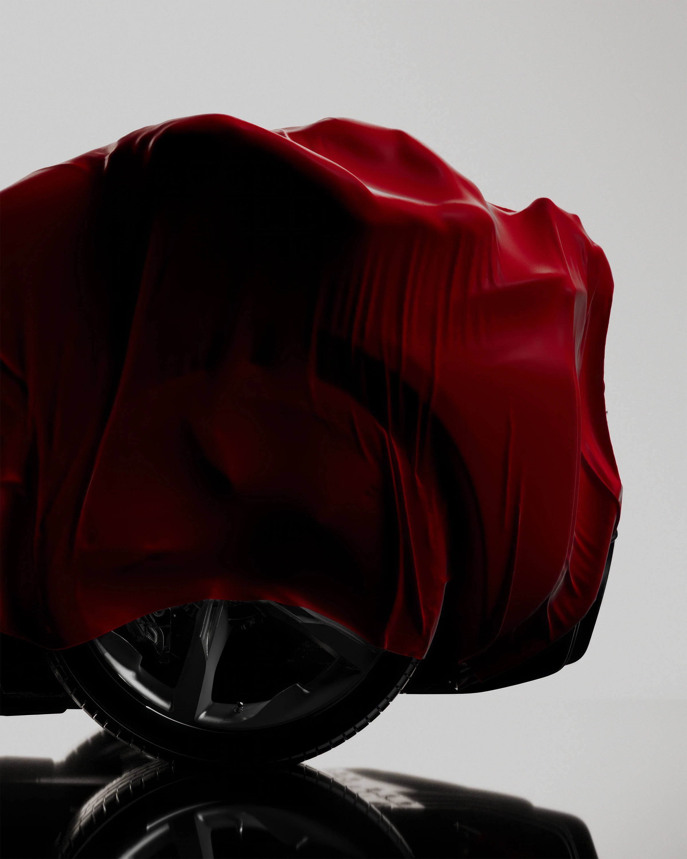 A vehicle is under a red fabric cover, with a focus on the tire, rim, and reflection against a bright white background.