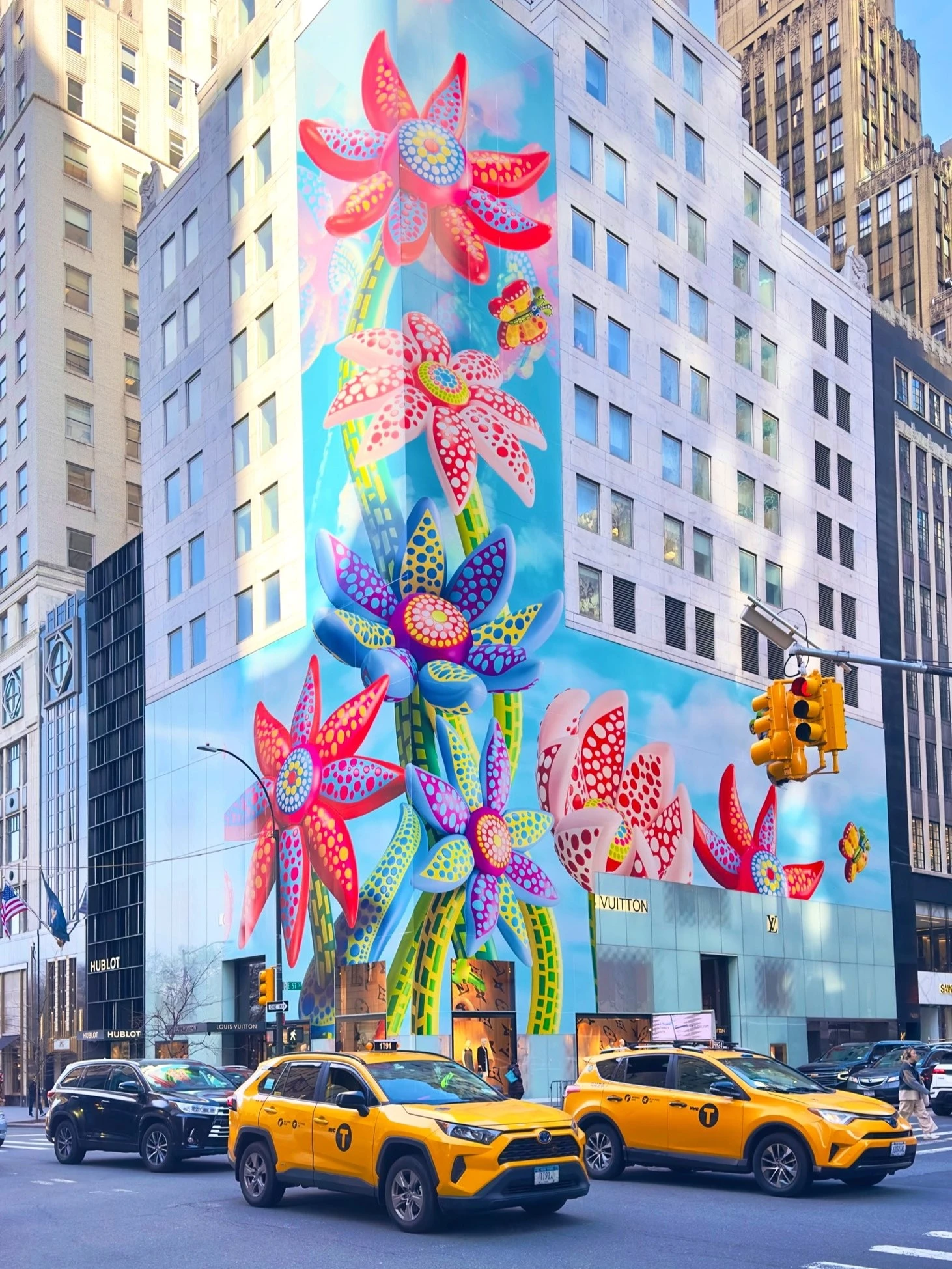 Eye-level shot of a building covered in floral artwork, with yellow taxis and other cars on the street in an urban environment.