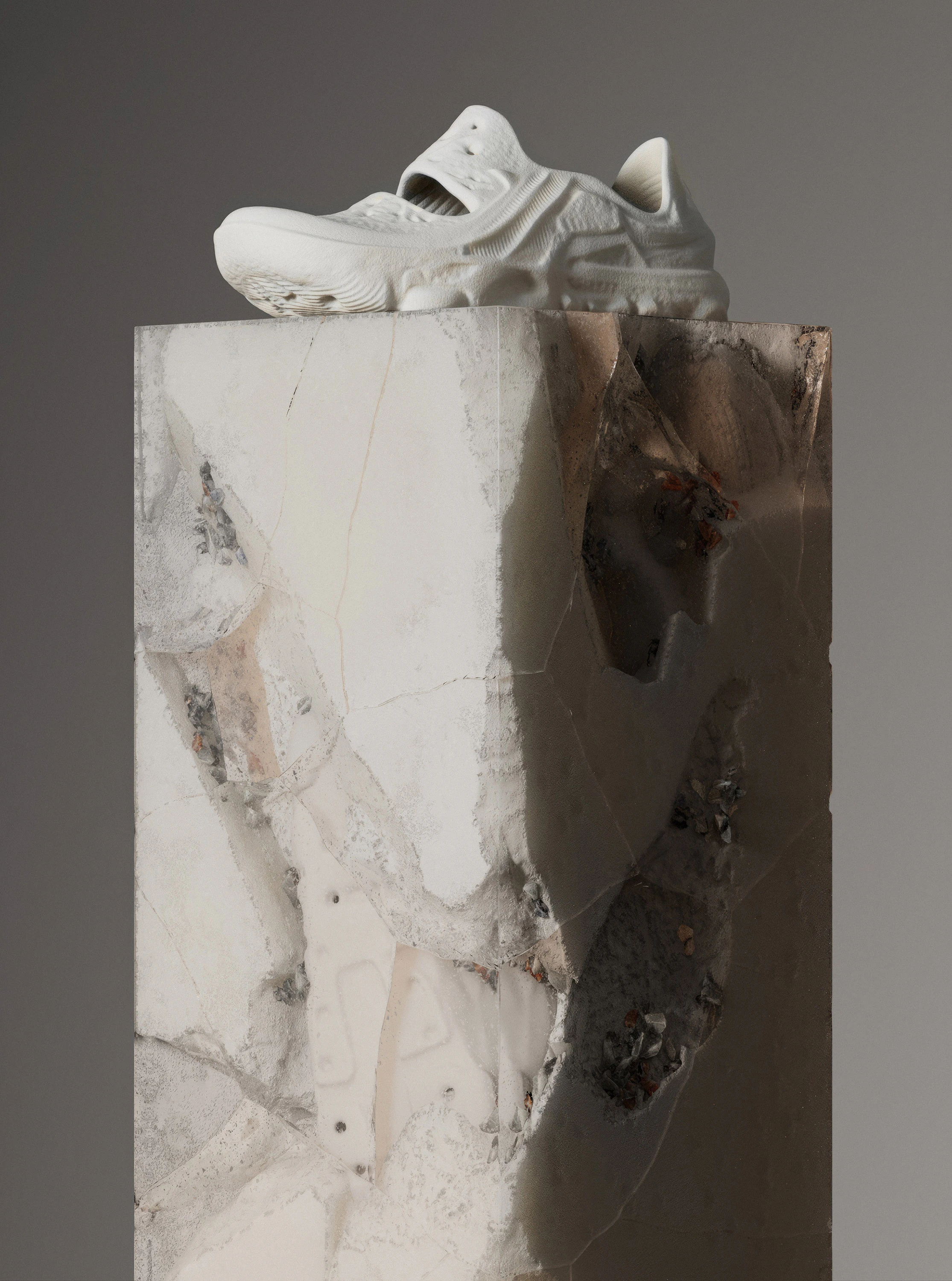 Studio shot of a modern white running shoe on a marble plinth with intricate grey veining against a neutral grey backdrop.