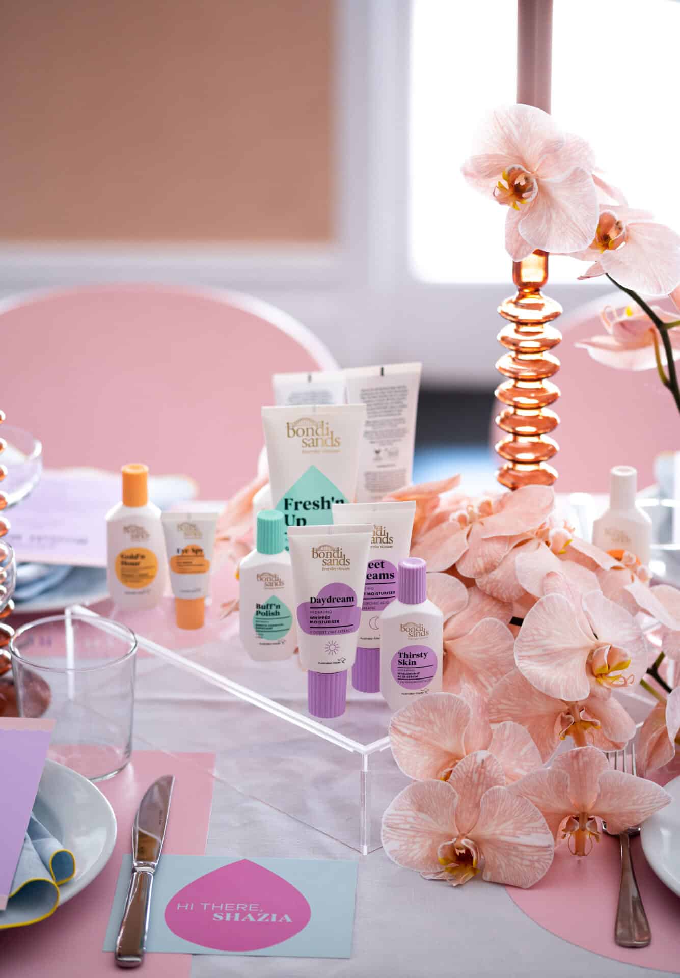 Table setting with skincare products by Bondi Sands, floral arrangements, and place cards, styled in soft pink and white tones.