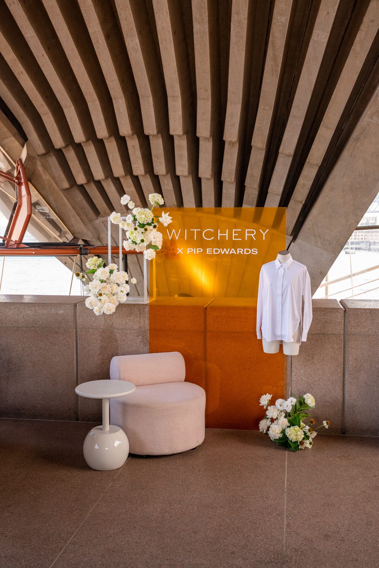 Display at Witchery x Pip Edwards event with white shirt on a mannequin, round chair, white flowers and architectural concrete backdrop.