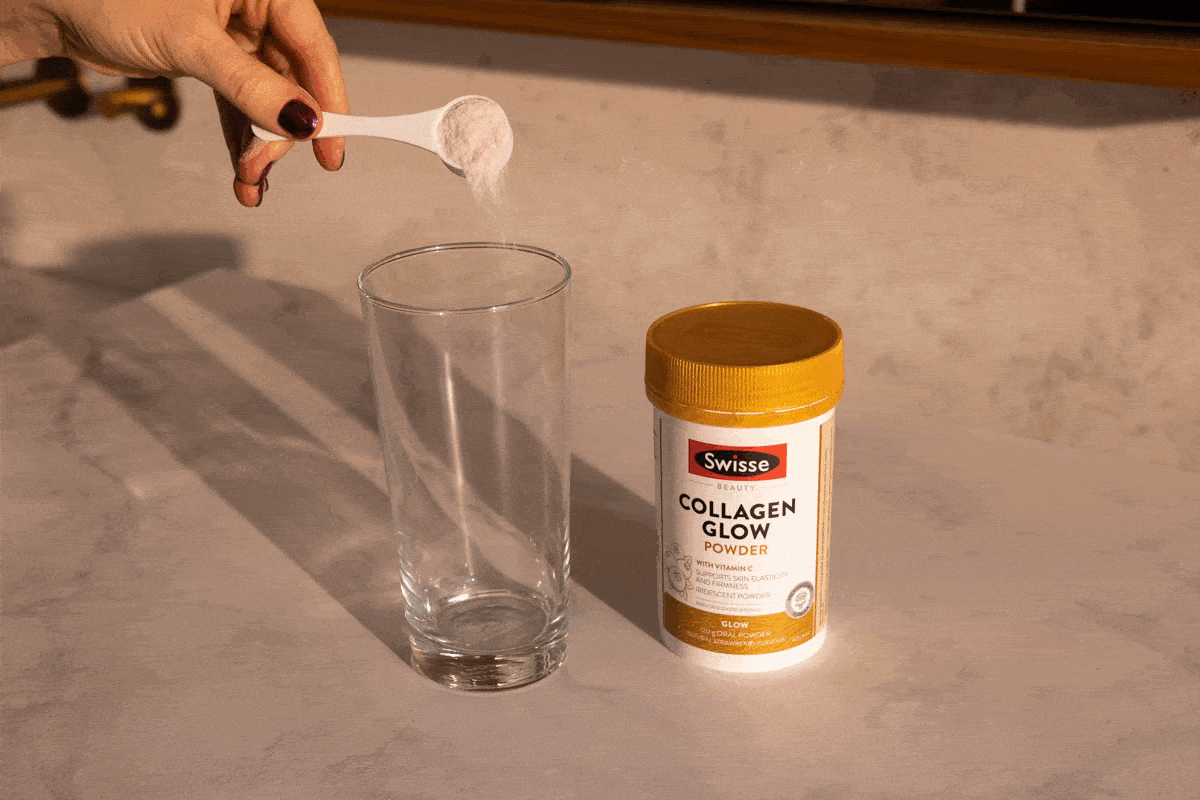 Collagen powder being poured from a white measuring spoon into a clear glass, with a container of Swisse Collagen Glow powder nearby.