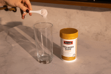 Hand pouring collagen powder from a small white spoon into a clear glass next to a Swisse Collagen Glow Powder container