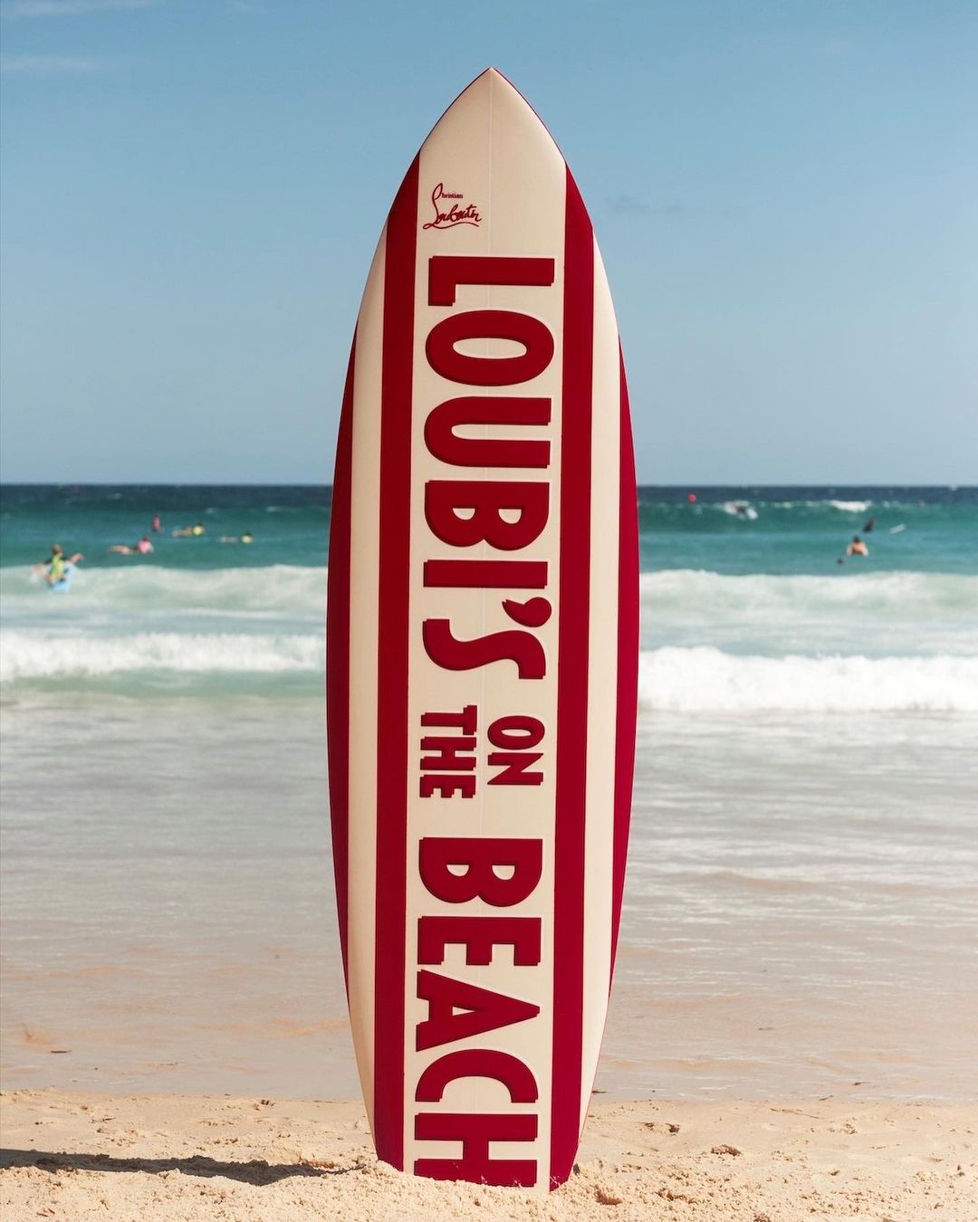 Striking image of a surfboard with 'Loubi's on the Beach' text, set against a vibrant beach scene with ocean and sky backdrop.