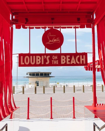 A vibrant red beach installation featuring signage reading Loubi's on the Beach framed by a structure overlooking the ocean.
