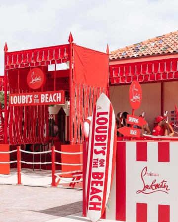 Red and white striped beach cabana installation with a surfboard displaying the text Loubi's on the Beach in Sydney.