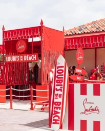 Red and white striped beach cabana installation with a surfboard displaying the text Loubi's on the Beach in Sydney.
