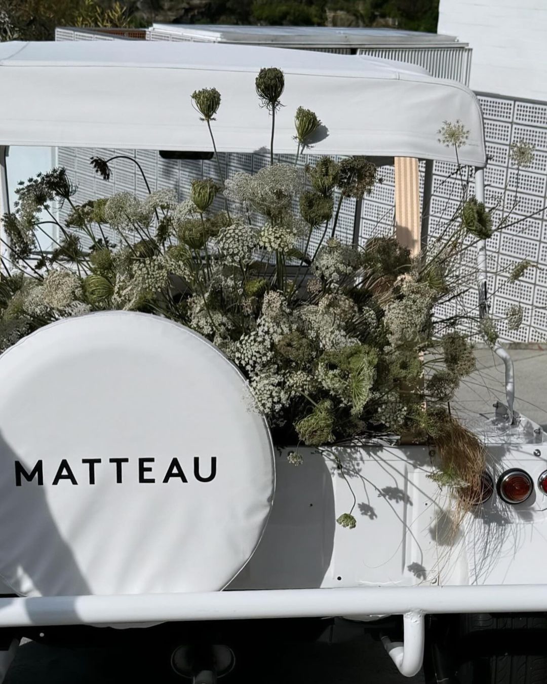 White vehicle decorated with white flowers and foliage, featuring a visible spare tire cover with the text MATTEAU printed.