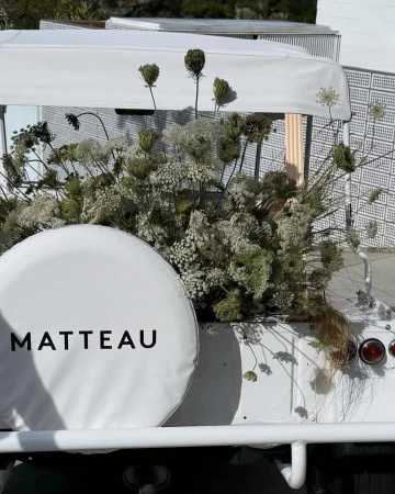 White vehicle decorated with white flowers and foliage, featuring a visible spare tire cover with the text MATTEAU printed.