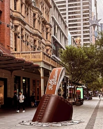 Giant leather boot sculpture installation on a pedestrian city street in Sydney with historic buildings.