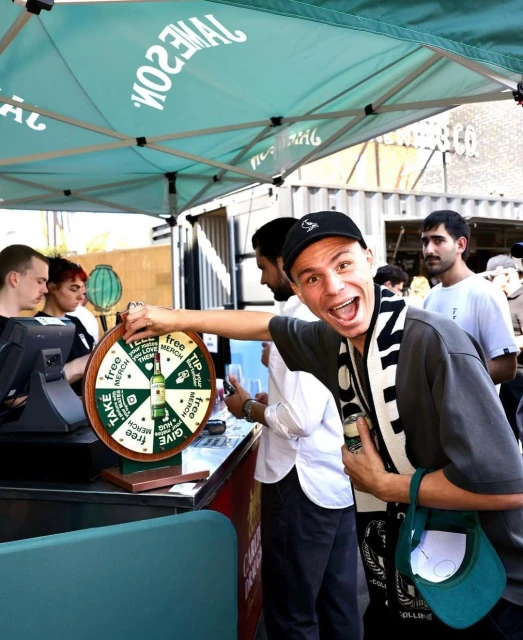 Enthusiastic man spinning a prize wheel at an outdoor Jameson Irish Whiskey promotional event, with blurred people in the background.