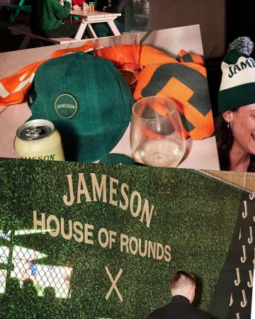 Indoor promotional shot with Jameson Irish Whiskey branding displayed on a grass-covered wall, canned beverages, hats and other branded items.