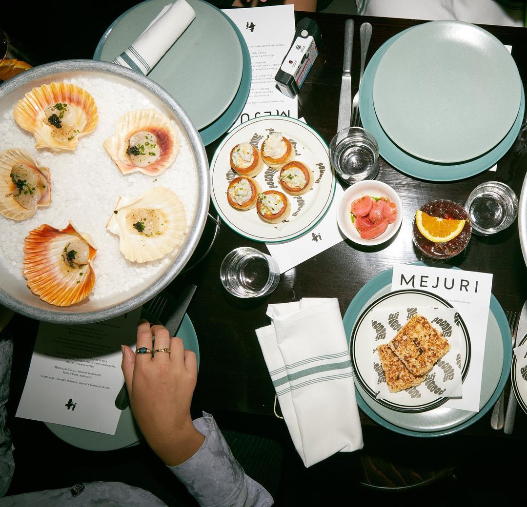 Overhead shot of a table with plates of scallops, appetizers, drinks, and neatly folded napkins in a restaurant setting.