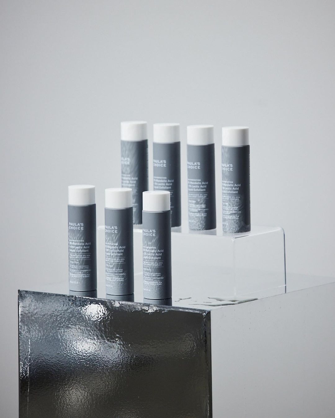 Paula's Choice skincare products displayed on mirrored platforms against a soft gray background in a beauty product shot.