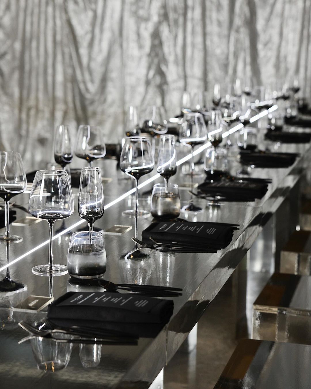 Elegant table setting with crystal glasses, black napkins, and silverware arranged for a formal event, reflecting modern design.