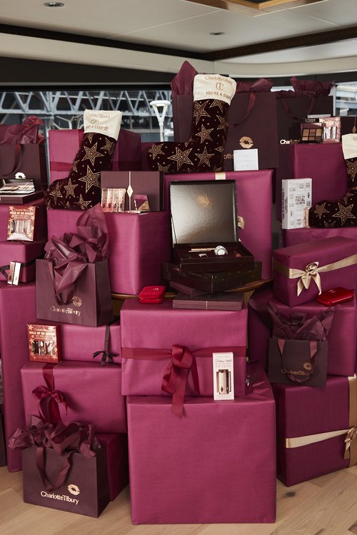 Stack of wrapped gifts with Charlotte Tilbury branded shopping bags and stockings in a maroon and gold color scheme.