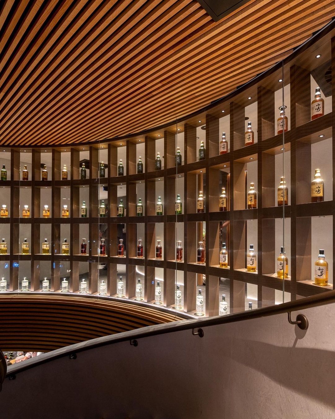 Display of liquor bottles on shelves with a curved wooden ceiling and a metal railing in the foreground.
