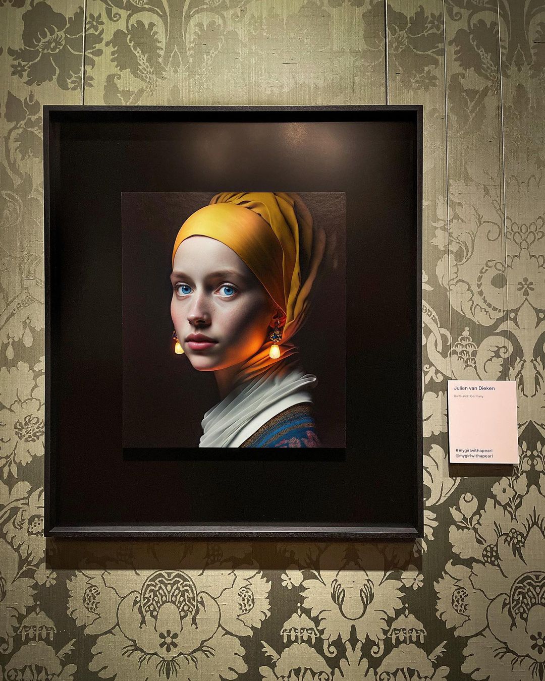 Artwork framed on a patterned wall depicts a young woman in a yellow headscarf and ornamental earrings. Soft lighting enhances the image.