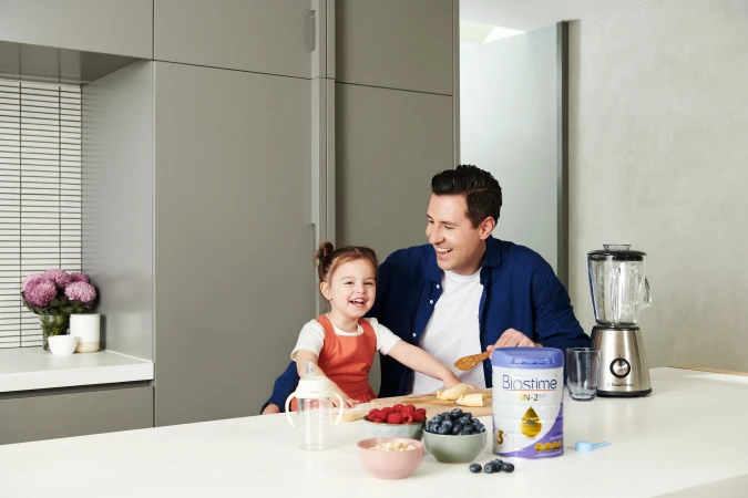 A happy father and daughter prepare a smoothie together at home with fresh fruit and a blender in a bright and modern kitchen.