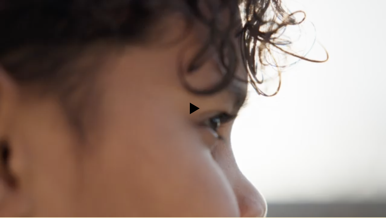 Close-up of an adult with curly hair looking off to the right against a bright, blurred background, shallow depth of field, and head and shoulder shot.